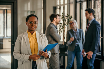 Portrait of a corporative businesswoman standing in the office, people in the background talking.