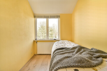 a bedroom with a blanket on the bed, and a window in the corner to the room is bright yellow