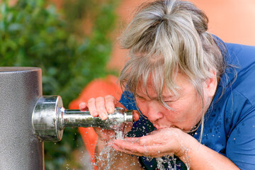Woman with white hair drinking water from a fountain splashing in her face