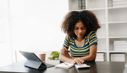  Beautiful African woman using laptop and tablet while sitting at her working place. Concentrated at work in home office