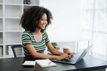  Beautiful African woman using laptop and tablet while sitting at her working place. Concentrated at work in home office