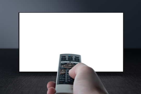 Television on gray wall and remote control in hand. Watching online TV. TV 8K flat screen oled with White blank screen. TV mockup.