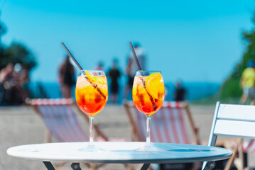 Two glasses of orange spritz aperol drink cocktail on table outdoors with sea and trees view...