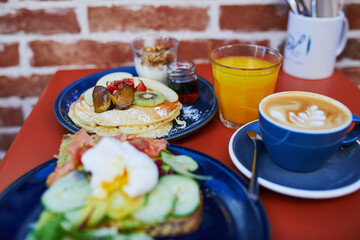 Delicious brunch with avocado and salmon toast, boiled egg, pancakes with fruits and coffee in cafe of Paris, France