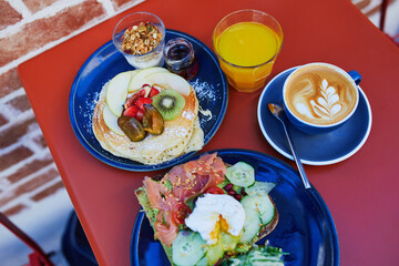 Delicious brunch with avocado and salmon toast, boiled egg, pancakes with fruits and coffee in cafe...