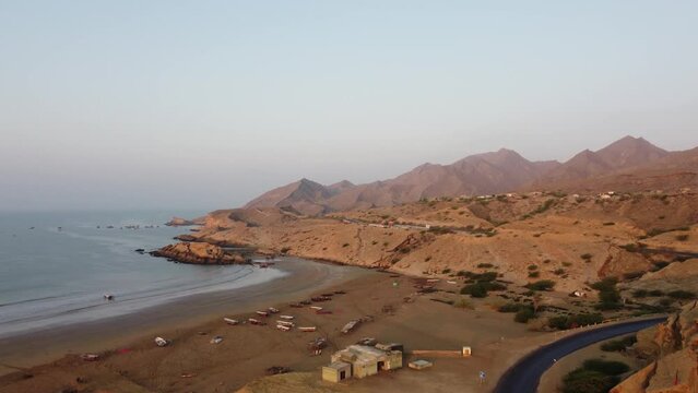 Aerial drone tilt up shot over Kund Malir Beach alongside a road beside Ormara Hingol national park with mountain range in the background in Balochistan.
