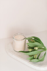Candle in glass, alstroemeria flower on white background. Copy space. Home decor, beauty treatments concept.