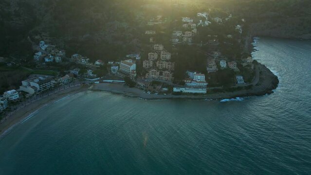 Waves crashing on mountain coast in Soller Mallorca Spain at sunset on hot summer evening with luxury hotels and villas