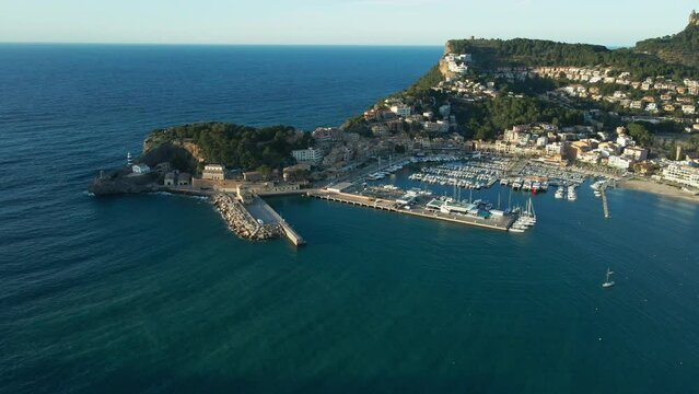 Spanish marina Soller port at sunset with boats, blue ocean and lush green mountains aerial panning shot