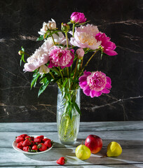 A beautiful still life with peonies in a vase and fruit on a dark marble background
