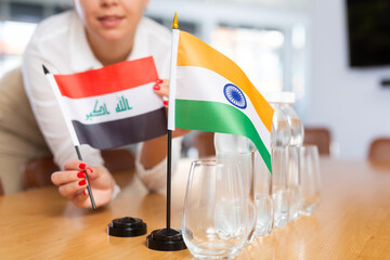 Employee of delegation prepares negotiating table - sets up the flag of India and Iraq