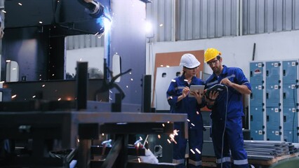 Two professional engineers control manage robot arm welding automation in heavy industry. Skillful man and woman working by welding robot together in steel factory