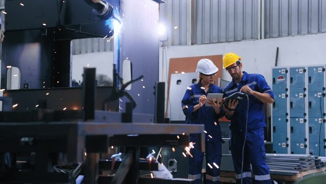 Two professional engineers control manage robot arm welding automation in heavy industry. Skillful man and woman working by welding robot together in steel factory