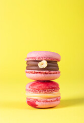 Two pink macarons with hazelnuts and caramel on yellow background, Vertical format