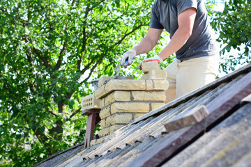 Bricklayer repair brick chimney on asbestos house rooftop