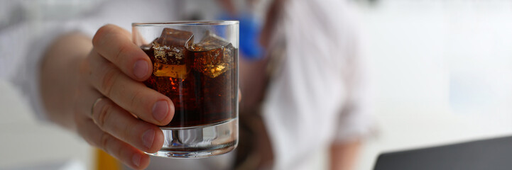 man holds a glass of cola and whiskey with ice in hand at workplace in office. Alcoholics and alcoholism in workplace
