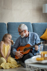 Grandfather plays guitar for her granddaughter while she  smile  	