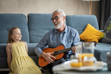 Little girl smiling and looking curiously at her grandfather as he plays guitar and sings for her