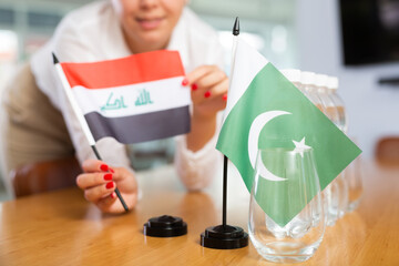 Little flag of Pakistan on table with bottles of water and flag of Iraq put next to it by positive young woman in meeting room