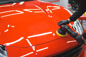 Professional car detailing expert using machine polish on a bonnet of a vivid red sports car....