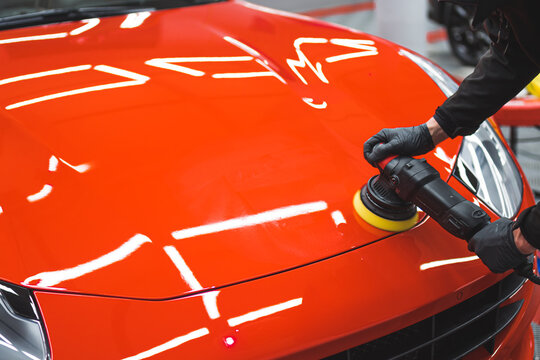 Professional car detailing expert using machine polish on a bonnet of a vivid red sports car. Specialistic equipment for polishing. High quality photo
