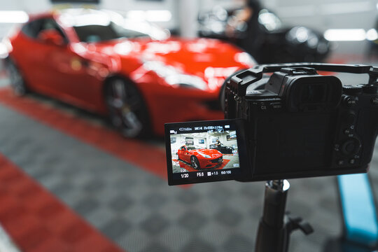 Professional car photo session at mechanic's or in car detailing studio. Digital photo camera taking picture of a red car. Blurred background. High quality photo