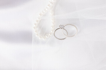 A pair of white gold engagement rings with a diamond on the the white veil of the bride and pearl...