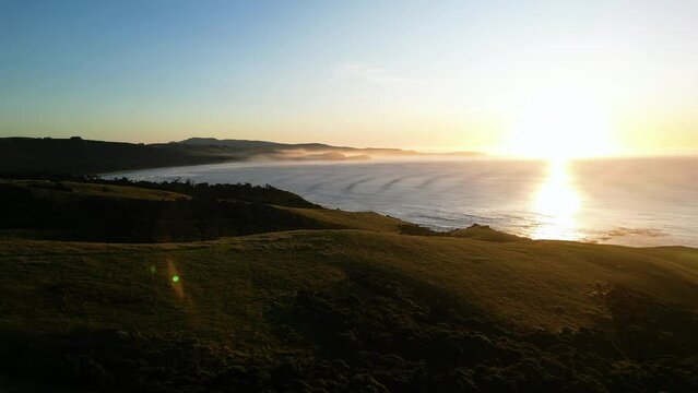 Cinematic drone shot of balclutha coastline during golden sunset with sun reflection on water in the evening, New Zealand