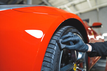 Closeup shot of blackening tires car detailing of a red sports car. Car detailing process. Cleaning tires with a sponge. High quality photo