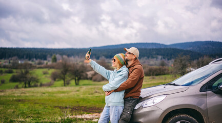 Romantic middle age couple hugging standing next to cars during auto travel in countryside. Taking...