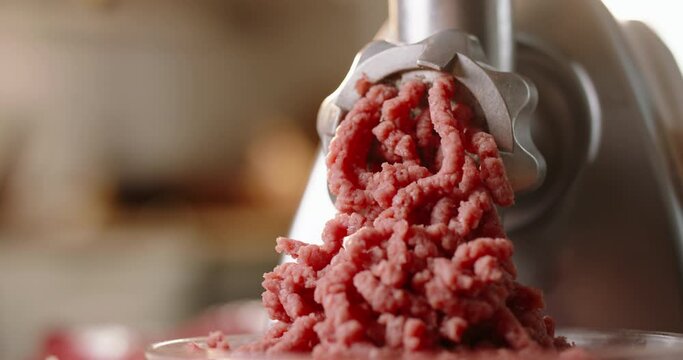 Meat coming through grinder plate. Closeup of minced meat flowing out of meat grinder. Blurred background kitchen. Advertising. Chef cook minced meat for burger. Home calm cooking food gourmet