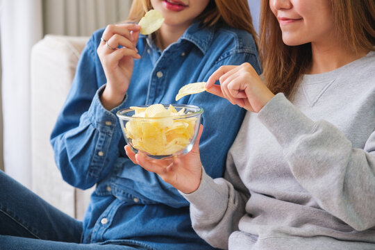 Closeup image of a young couple women sharing and eating potato chips together