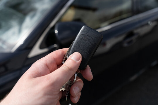 Hand Of Man Holding Remote Car Key, Next To A Black Vehicle.