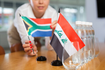 Employee of delegation prepares negotiating table - sets up the flag of South Africa and Iraq