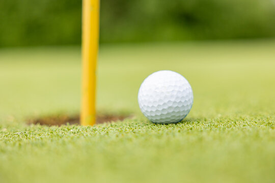 golf ball close to the hole with the flag still in close up selective focus