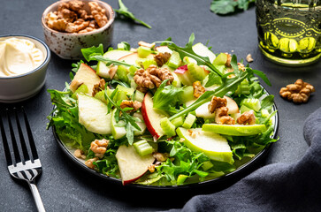 Waldorf salad with red and green apple, raw celery, lettuce, arugula and walnuts with mayonnaise dressing, black table background, top view
