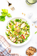 Waldorf salad with chicken fillet, red and green apples, raw celery, lettuce, arugula and walnuts on plate, white table background, top view