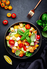 Panzanella salad with stale bread, colorful tomatoes, mozzarella cheese, onion, olive oil, salt and green basil, black table background, top view
