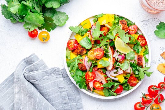 Gourmet salad with grilled chicken and mango salsa, tomato, cilantro, onion and lettuce in mexican style, white kitchen table background, top view