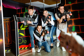 Ordinary Laser tag players young mens and womens playing in teams in dark laser tag station. High...