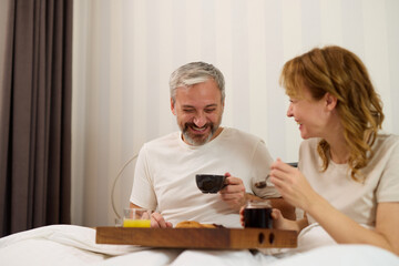 Mature couple enjoying coffee and breakfast at home in bed