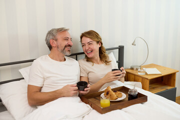 Mature couple enjoying coffee and breakfast at home in bed