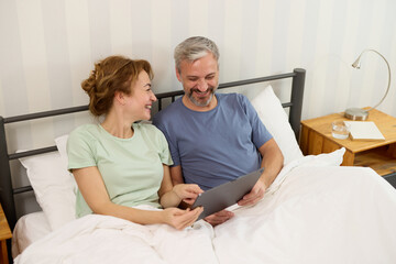 Smiling mature couple using digital tablet at home in bed