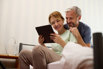 Smiling mature couple using digital tablet at home in bed