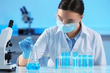 Scientist taking sample of light blue liquid and test tubes in laboratory