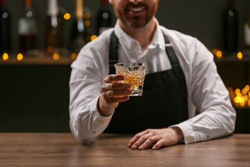 Bartender with glass of whiskey at bar counter indoors, closeup