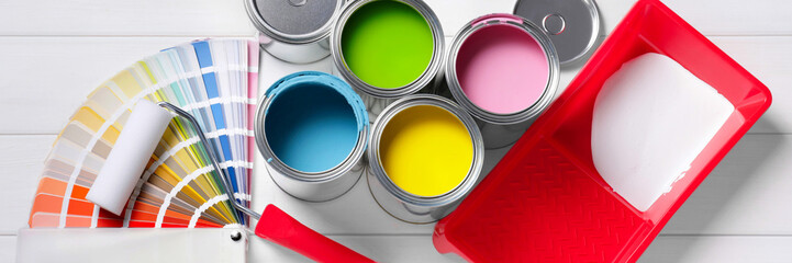 Cans of paints, roller, tray and palette on white wooden background, flat lay. Banner design