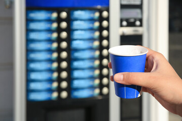 Woman with paper cup of beverage near coffee vending machine, closeup