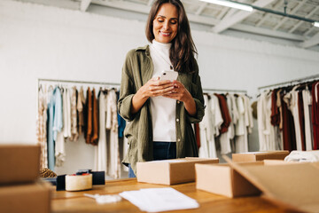 Female entrepreneur using a mobile phone as she processes clothing orders for shipping