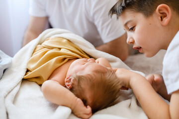 Older brother touches infant newborn in bed